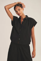 Woman wearing a black sleeveless blouse against a plain background