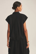 Woman wearing a black sleeveless dress against a plain background