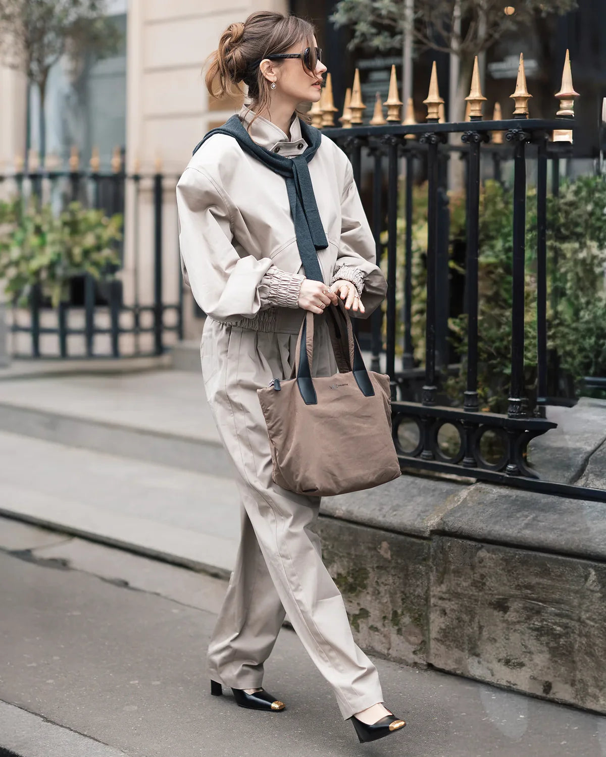 Woman walking on a sidewalk wearing a white shirt, beige pants, and carrying a brown bag.