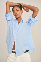 Woman wearing a light blue button-up shirt with rolled-up sleeves against a neutral background