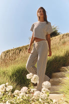 Woman in striped outfit standing on a grassy hill with flowers in the foreground