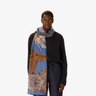 Person wearing a long, patterned scarf with a neutral background