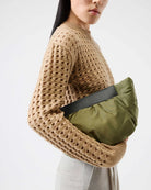 Person wearing a beige knit sweater holding an olive green bag against a white background
