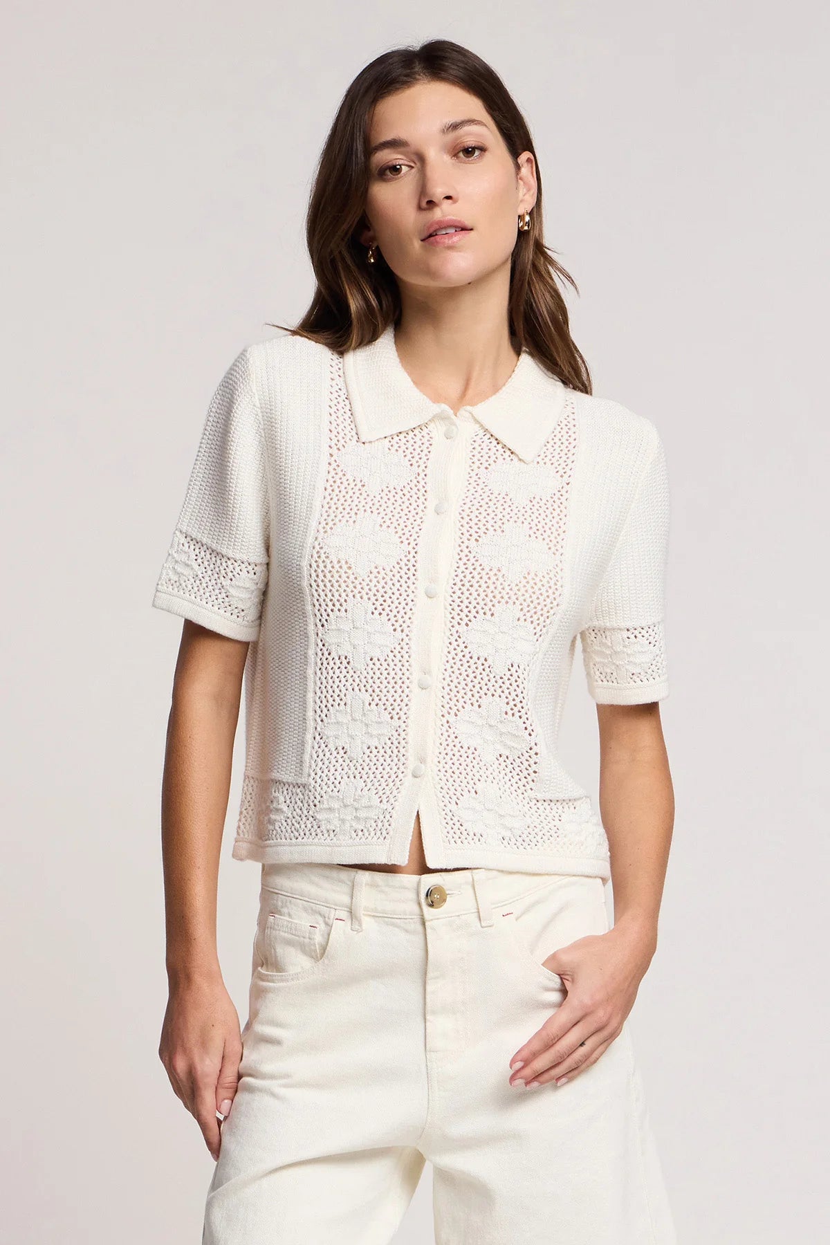 Woman wearing a white lace blouse and white pants against a plain background