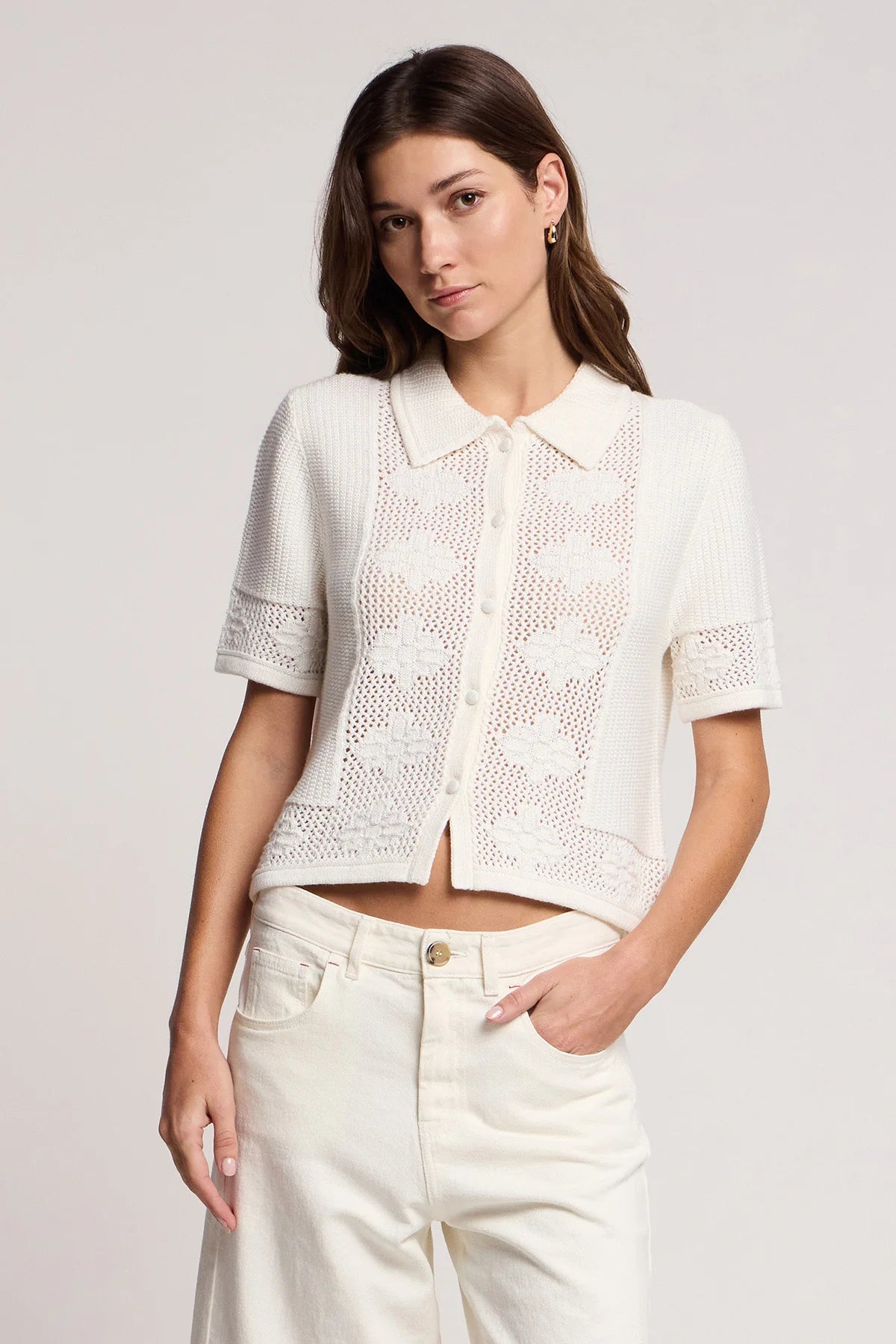 Woman wearing a white lace top and pants against a plain background