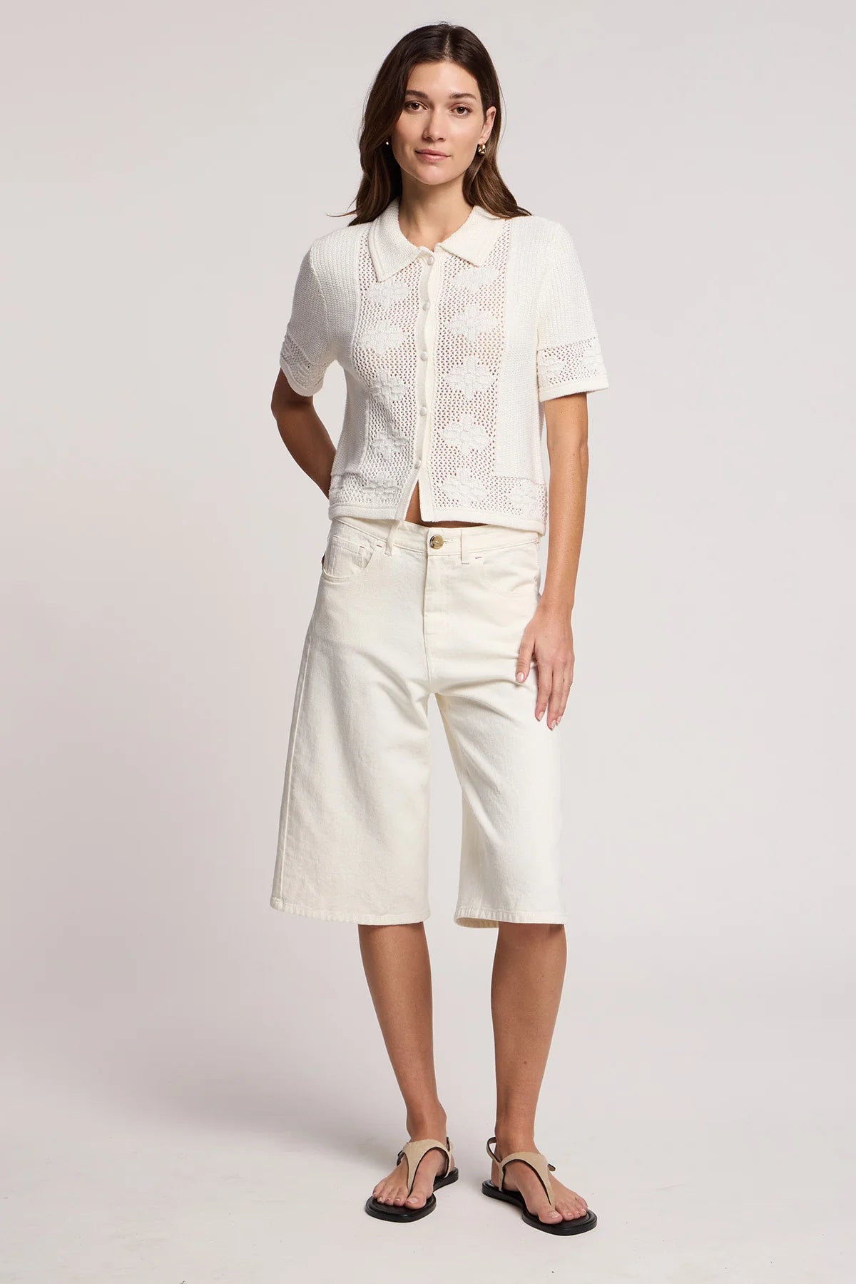 Woman wearing a white outfit with a short-sleeve top and long shorts on a plain background