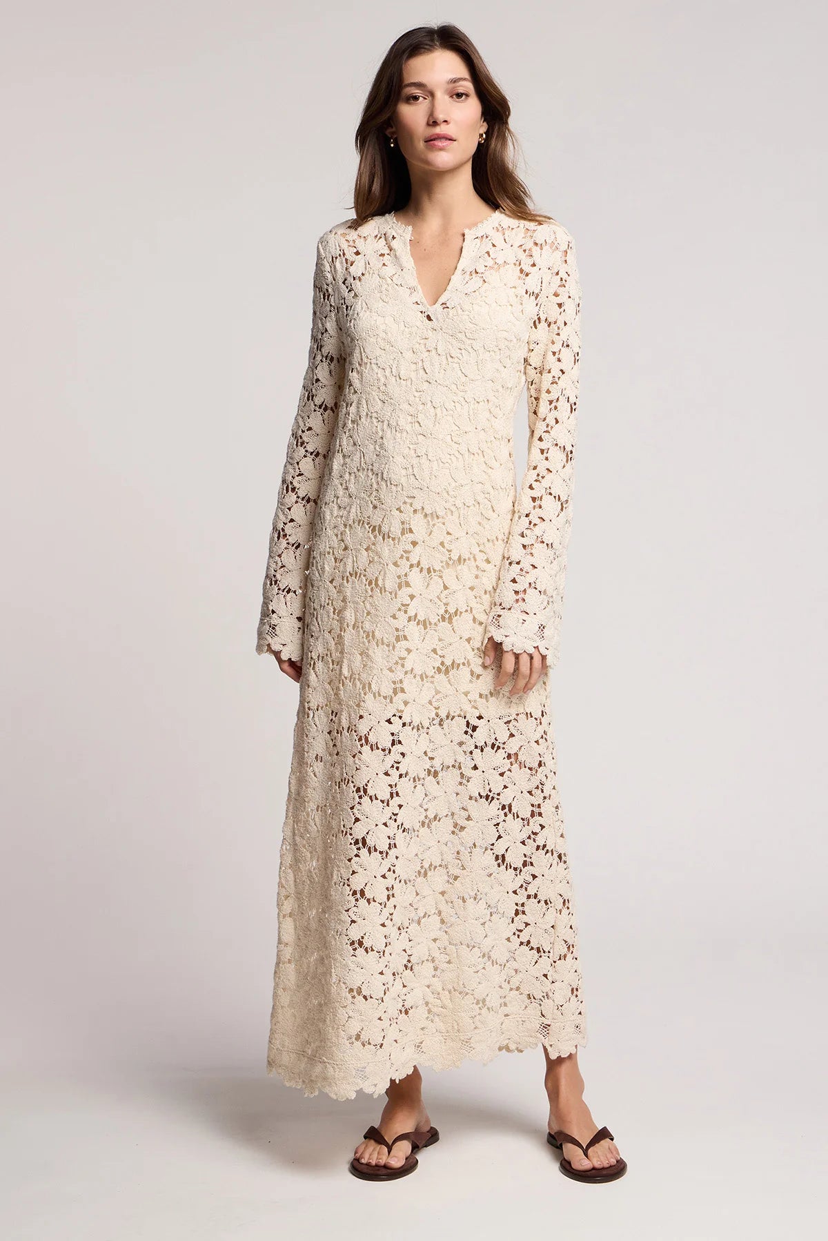 Woman wearing a long floral lace dress on a plain background