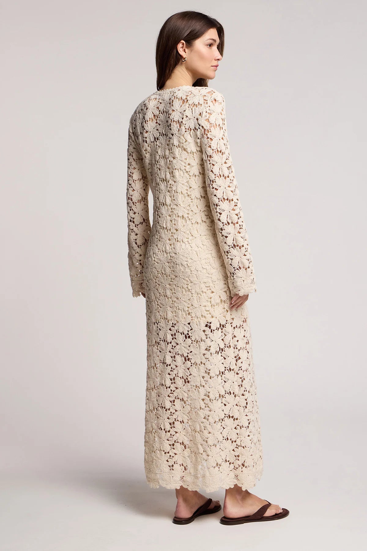 Woman wearing a long, light-colored floral dress against a plain background