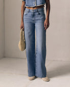 Person wearing blue jeans and a denim jacket holding a woven bag on a plain background
