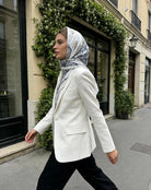 Woman wearing a white blazer and patterned scarf walking on a city street.
