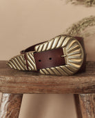 Brown leather belt with a large brass buckle on a wooden surface.