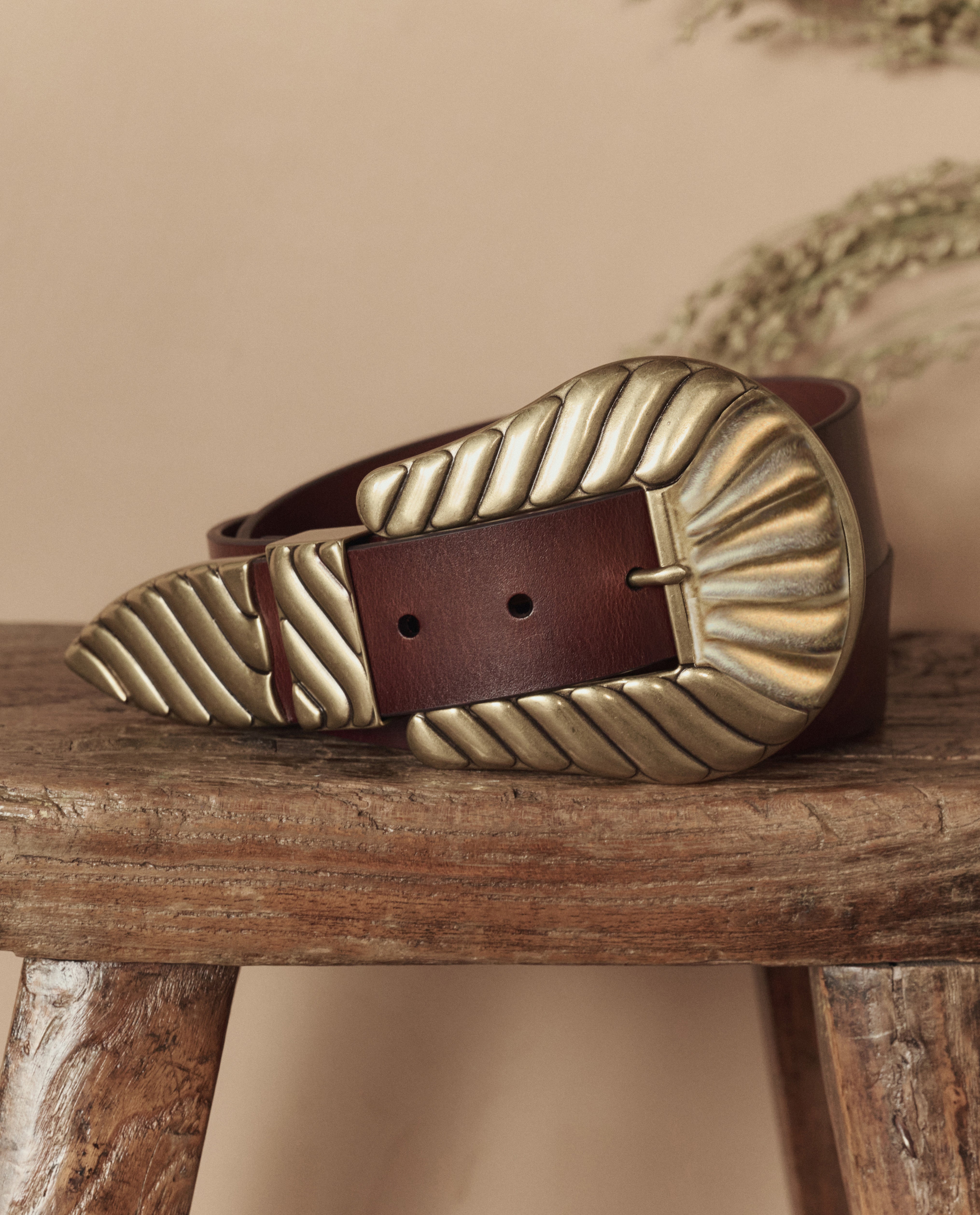 Brown leather belt with a large brass buckle on a wooden surface.