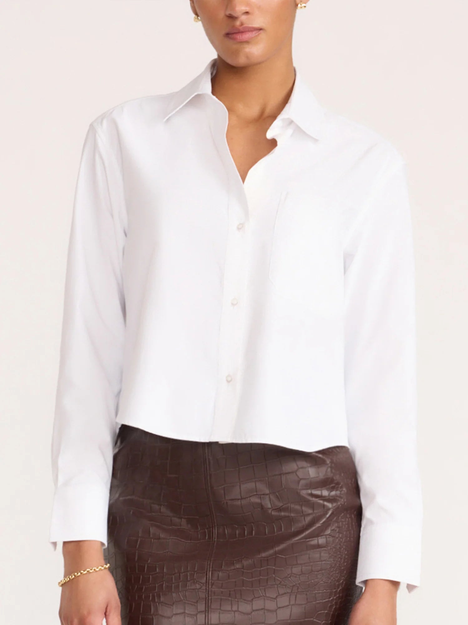 A woman wearing a white long-sleeve button-up shirt and a dark brown textured skirt, shown from the nose down against a plain light beige background.