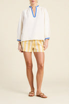 Woman wearing a white blouse with blue trim and yellow striped shorts on a beige background