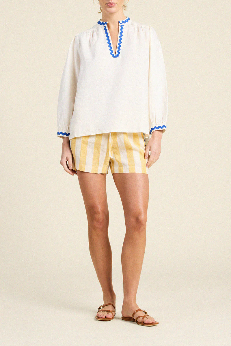Woman wearing a white blouse with blue trim and yellow striped shorts on a beige background