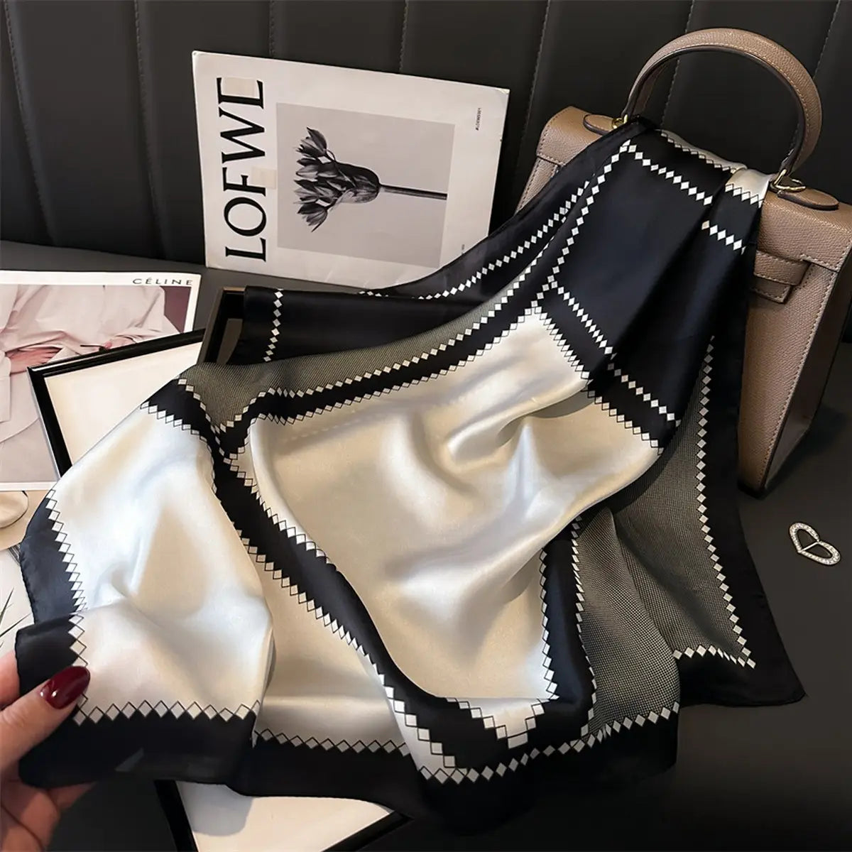 Black and white patterned fabric held by a hand with a magazine and handbag in the background.