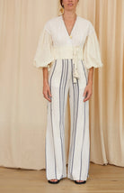 Person wearing a white blouse with bell sleeves and striped pants against a beige curtain background