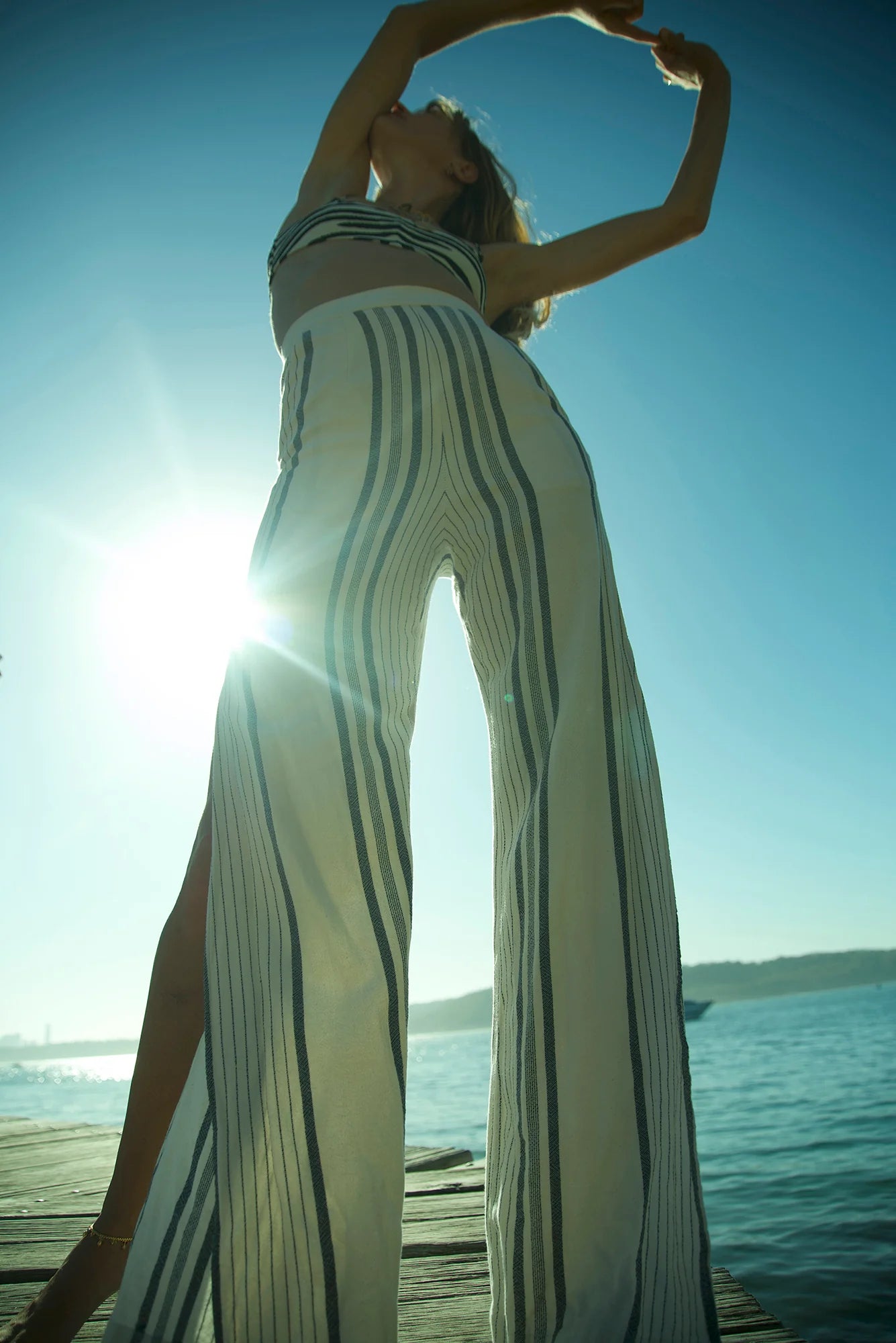 Woman in a long, striped dress standing on a dock with water and sky in the background