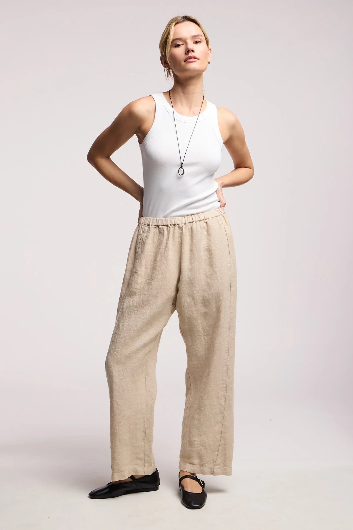 Woman wearing a white tank top and beige pants on a plain background