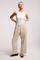 Woman wearing a white tank top and beige pants on a plain background