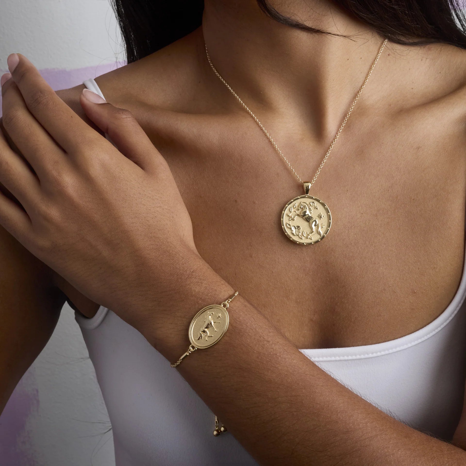 Gold necklace and bracelet with coin-like pendants on a person wearing a white top.