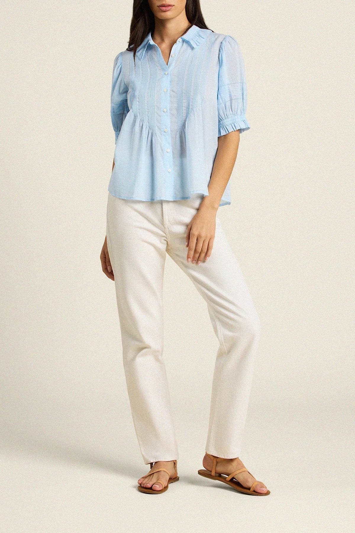 Woman wearing a light blue blouse and white pants on a beige background