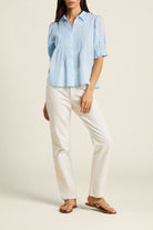 Woman wearing a light blue blouse and white pants on a beige background