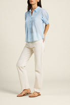 Woman wearing a light blue shirt and white pants on a beige background