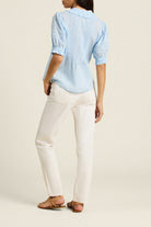 Person wearing a light blue shirt and white pants on a plain background
