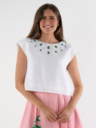 Woman wearing a white top with green patterns and a pink skirt on a white background