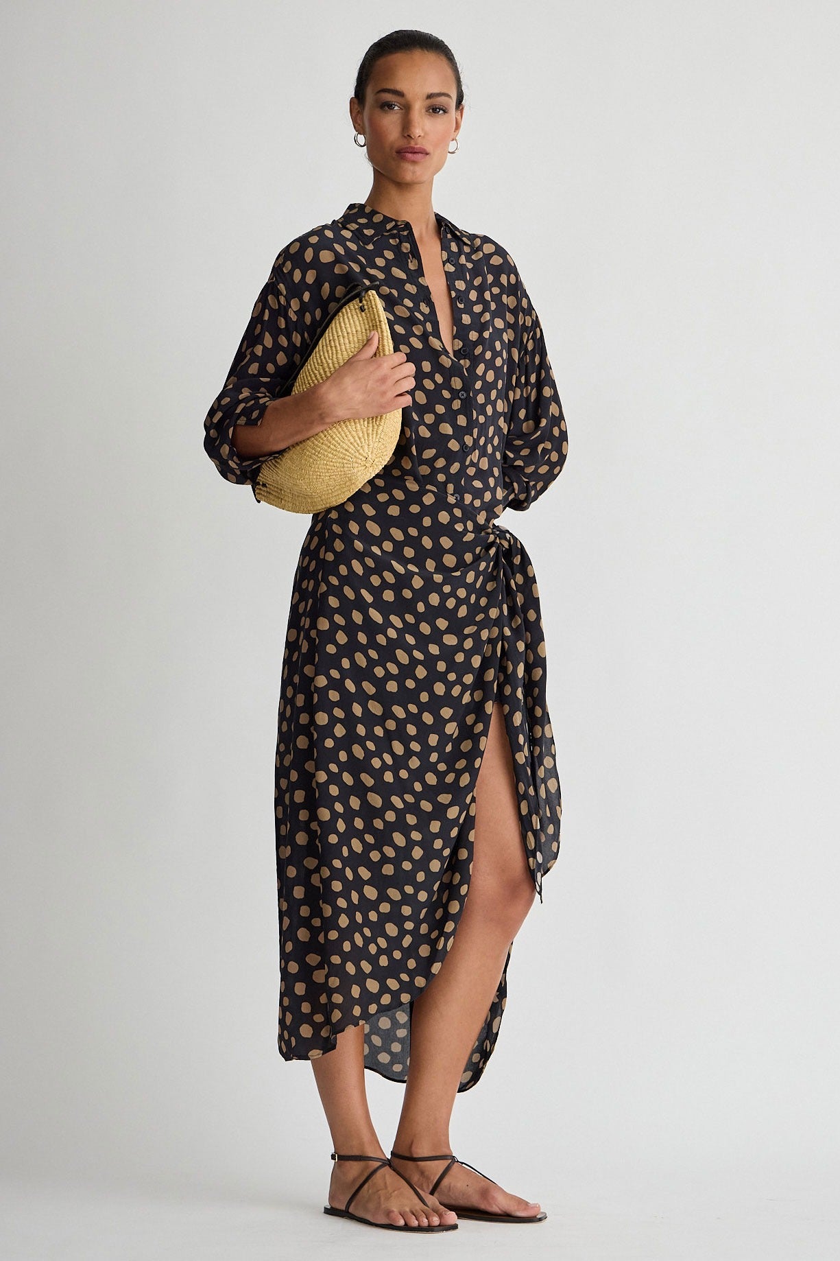 Woman wearing a patterned dress holding a yellow clutch against a white background