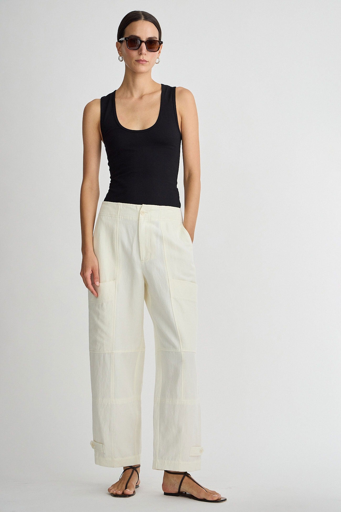 Woman wearing a black tank top and white pants on a plain background
