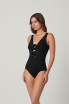 Woman wearing a black one-piece swimsuit with lace-up details on a light gray background