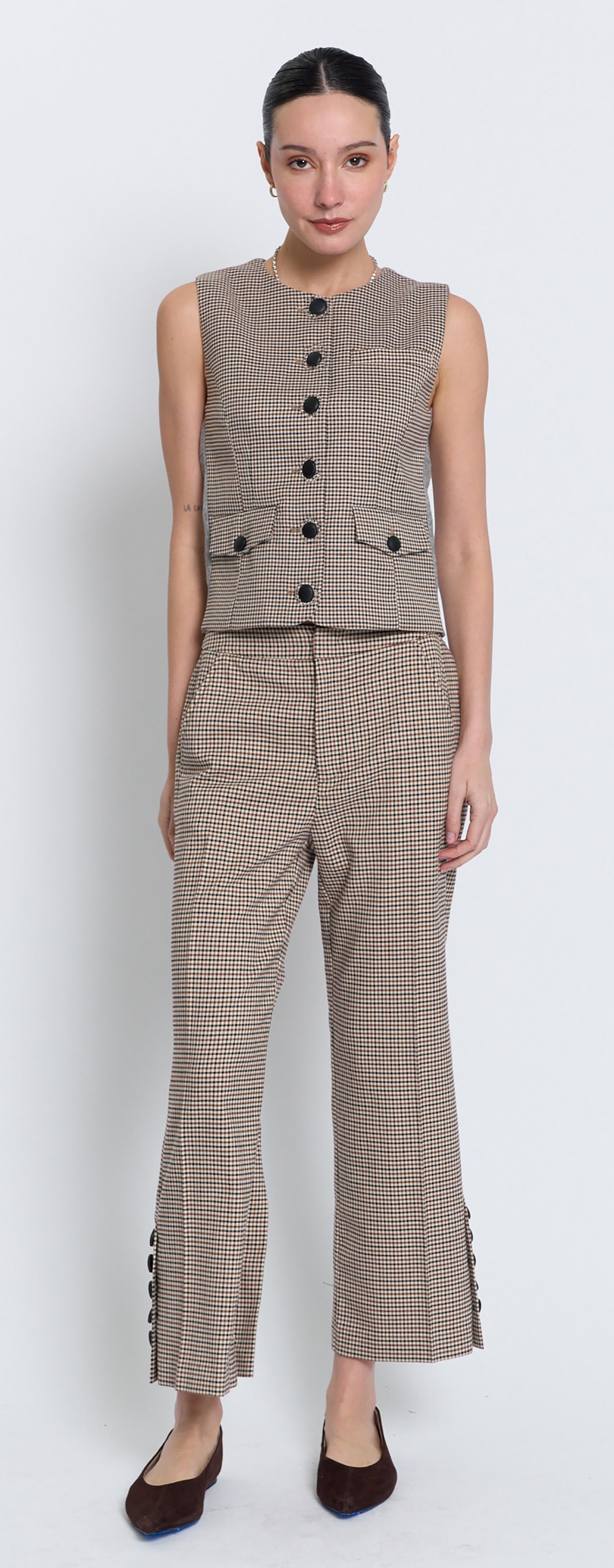 A model wearing a matching beige and brown checkered two-piece set consisting of a sleeveless button-front vest and cropped wide-leg trousers with button details at the hems, paired with dark brown flats.