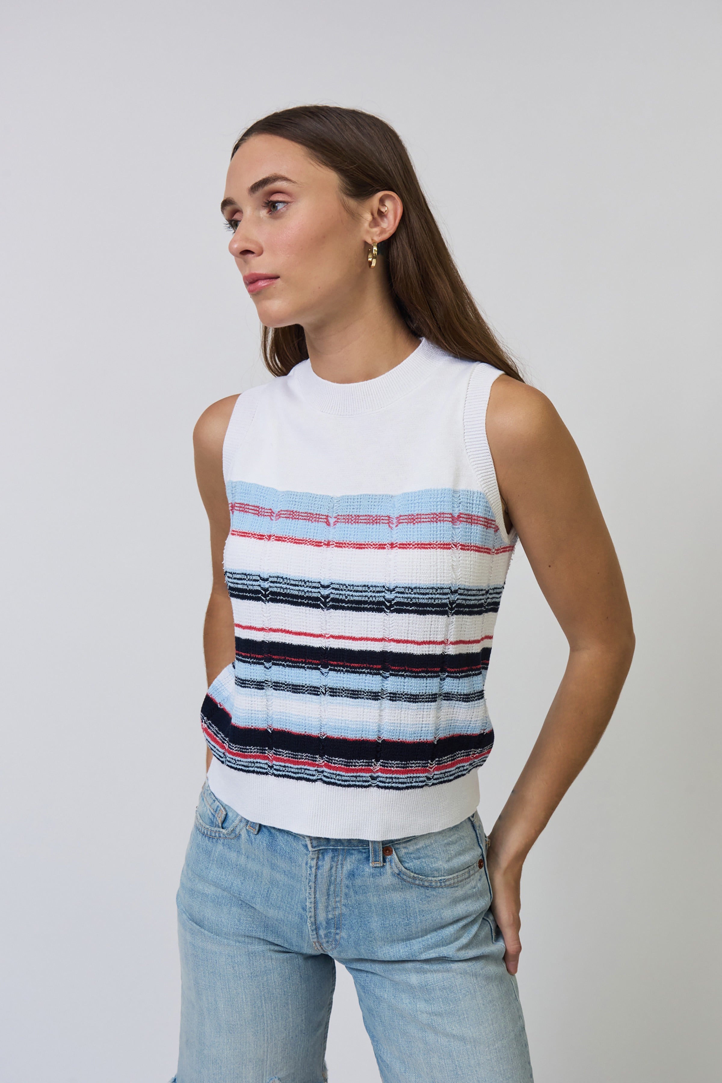 Woman wearing a sleeveless striped top and jeans against a plain background
