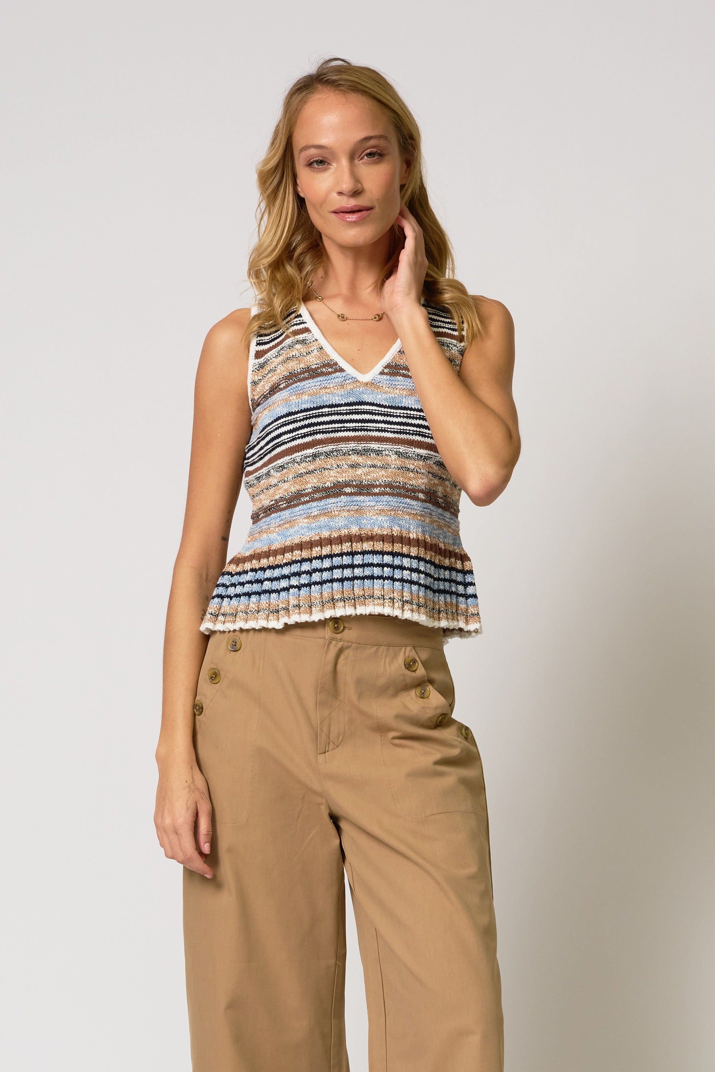 Woman wearing a striped sleeveless top and beige pants against a plain background