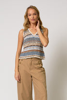 Woman wearing a striped sleeveless top and beige pants against a plain background