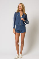 Woman wearing a blue tracksuit with white accents on a plain background
