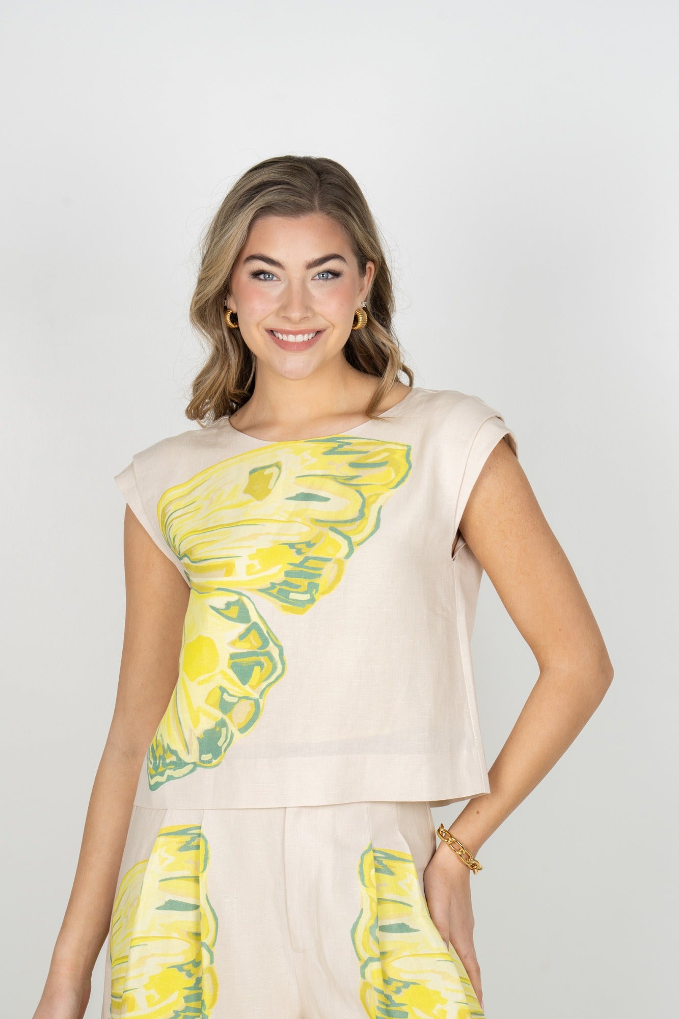 Woman wearing a beige sleeveless top with yellow floral patterns on a plain background