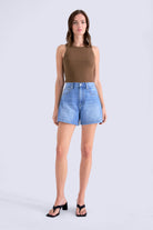 Woman wearing a brown sleeveless top and blue denim shorts on a white background