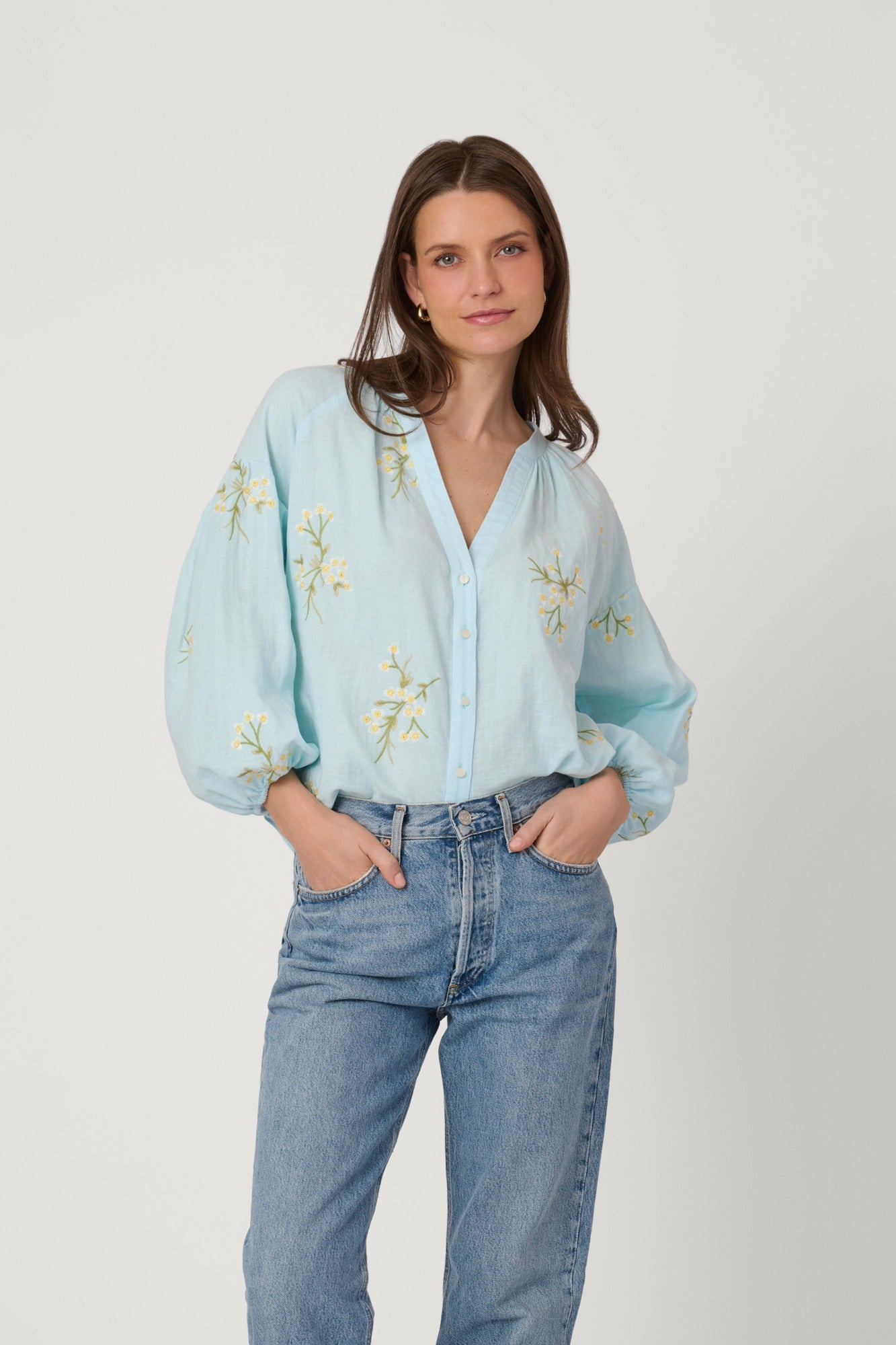 Woman wearing a light blue embroidered blouse and jeans on a white background