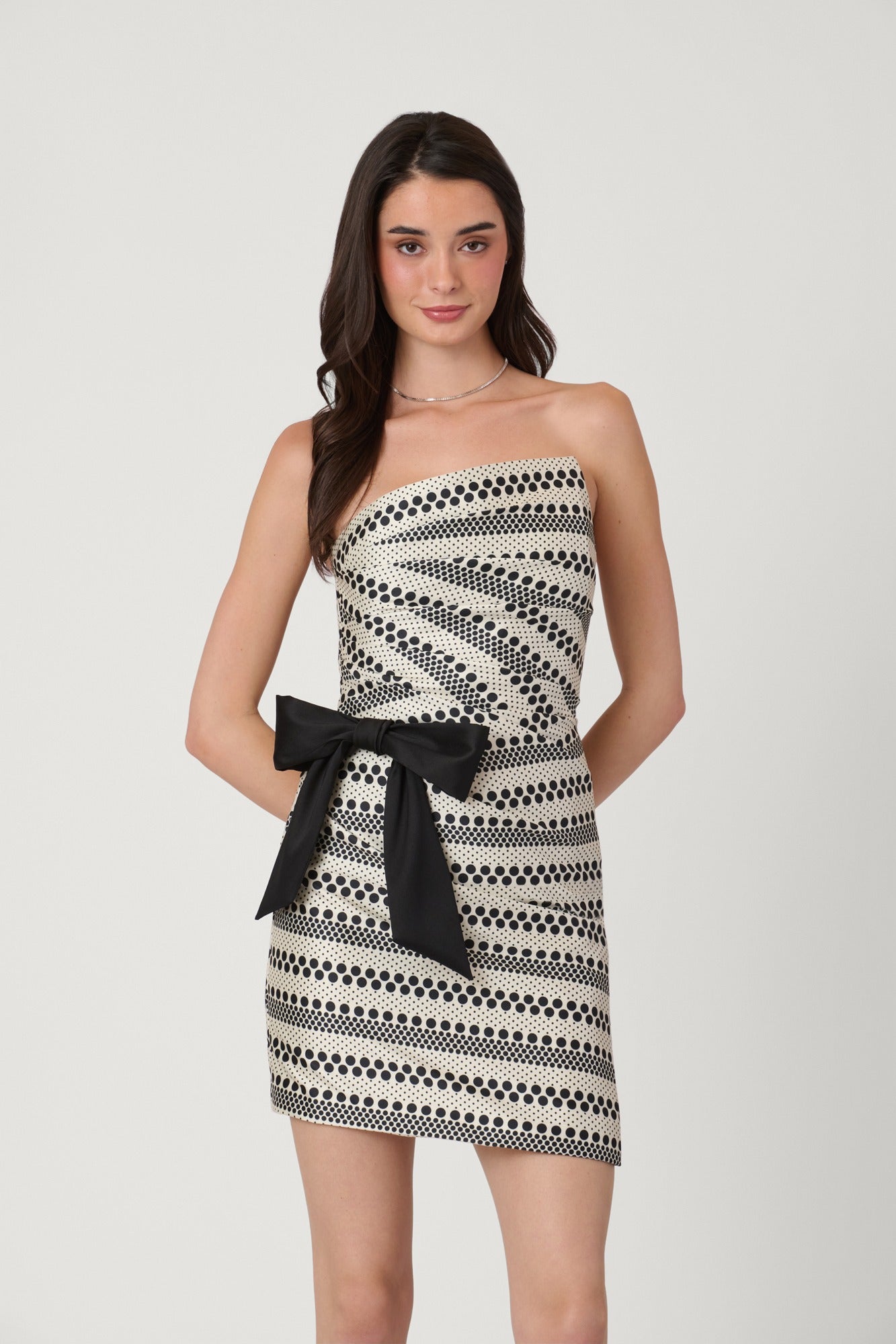 Woman wearing a strapless dress with black and white pattern and black bow on a light gray background