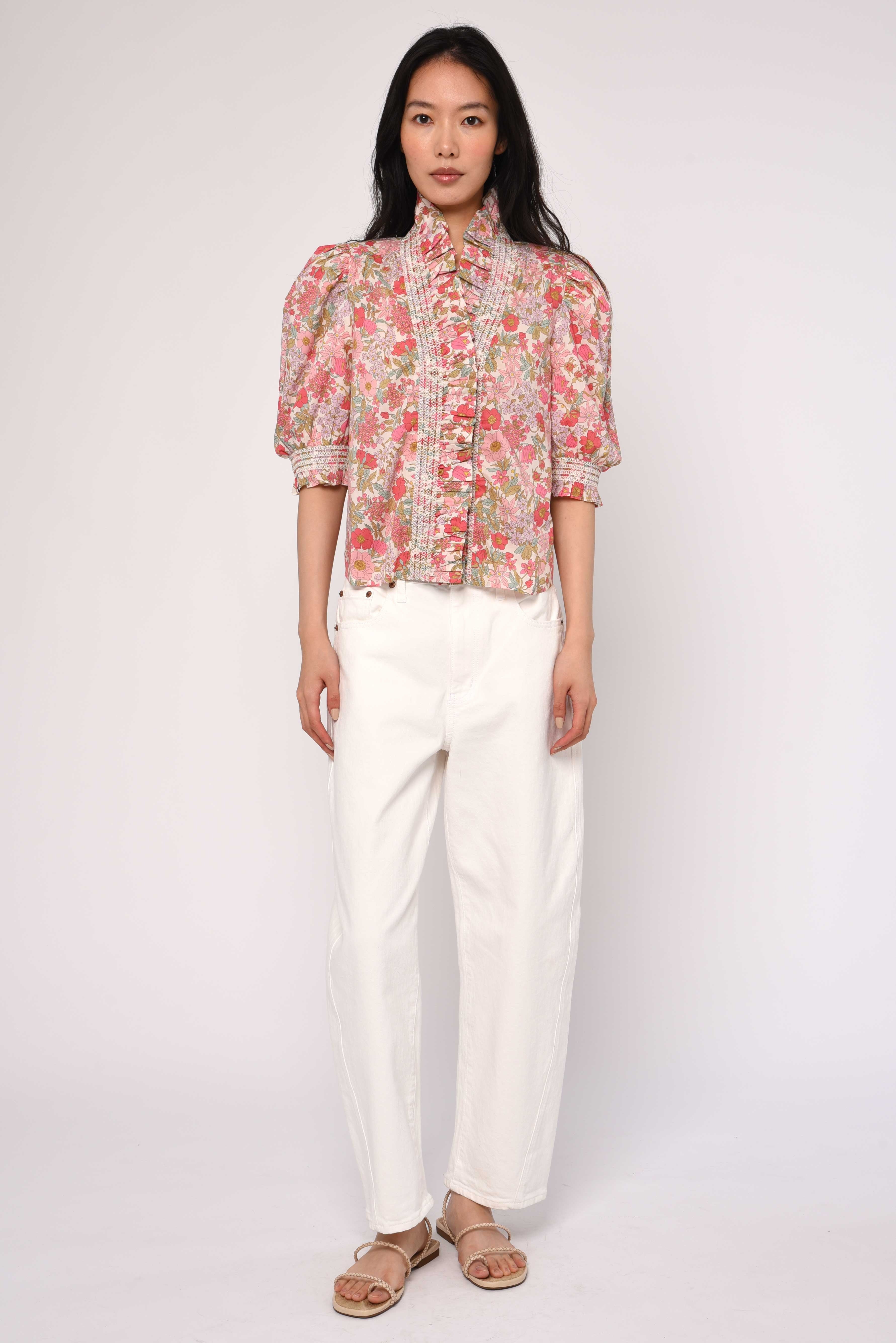Woman wearing a floral blouse and white pants on a plain background