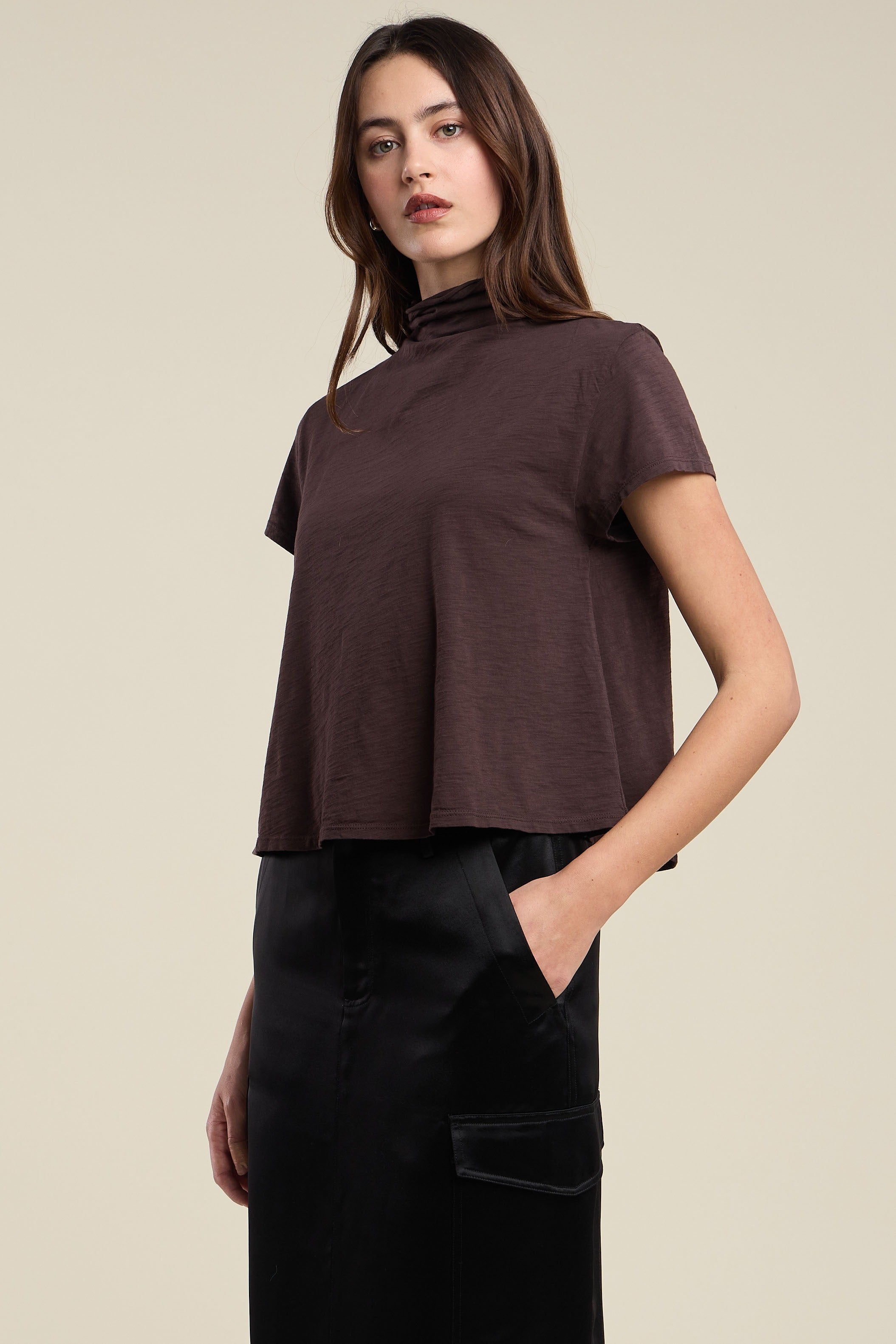 Woman wearing a brown top and black pants against a beige background