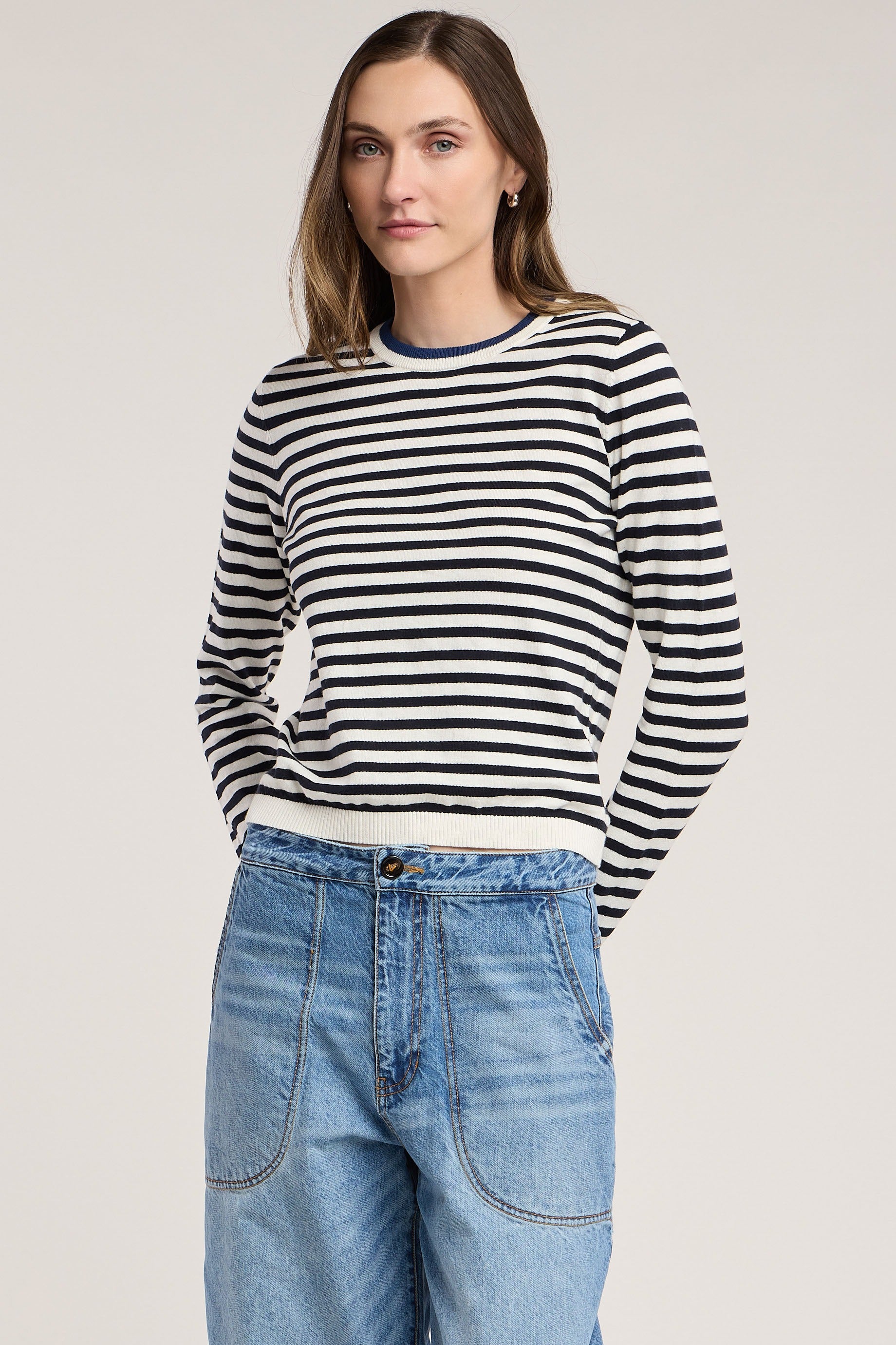 Woman wearing a black and white striped sweater and blue jeans on a plain background