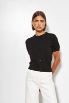 Woman wearing a black short-sleeve shirt and white pants against a white background