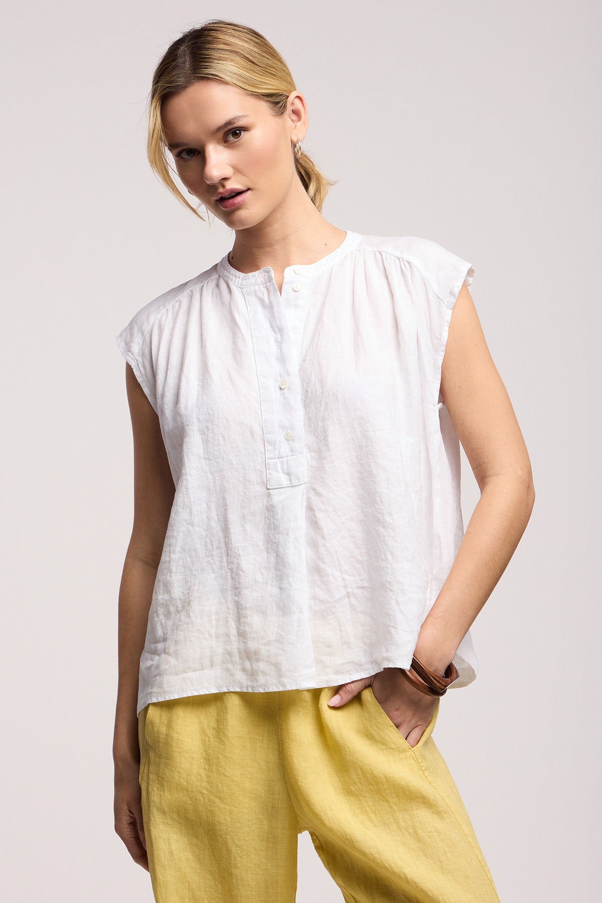 Woman wearing a white sleeveless top and yellow pants on a light background