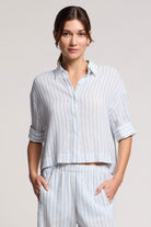 Woman wearing a light blue striped shirt and pants on a plain background