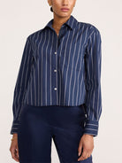 A model wearing a navy blue and white vertically striped cropped button-down shirt with dark navy pants, shown from the neck down against a plain light background.