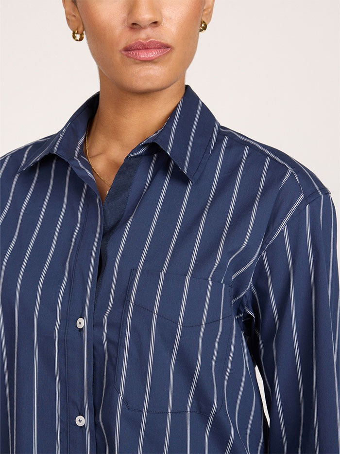 A close up of a model wearing a navy blue and white vertically striped cropped button-down shirt shown from the neck down against a plain light background.